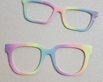 May include: Two pairs of rainbow glitter glasses. The glasses are a light pink, blue, yellow, and green color. The glasses are made of plastic and have a rounded shape.