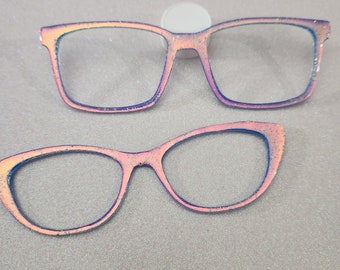 May include: Two pairs of iridescent glitter glasses, one with a square frame and the other with a cat-eye frame.