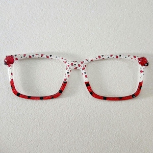 May include: White eyeglasses with a red and black ladybug pattern. The frame is made of plastic and has a square shape.