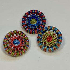 May include: Three round buttons with a woven design. The buttons are red, blue, and green.