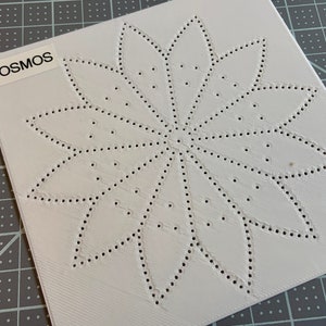 May include: A white square piece of paper with a design of a flower with a dotted outline. The word "COSMOS" is printed on the top left corner of the paper.