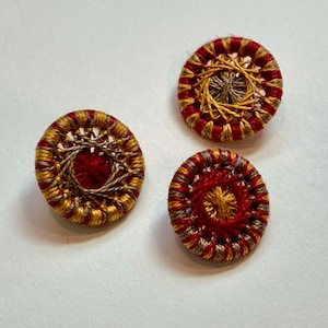 May include: Three round buttons with a red, gold, and brown woven design.