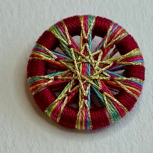 May include: A red button with a starburst design made of colorful threads and gold metallic thread.