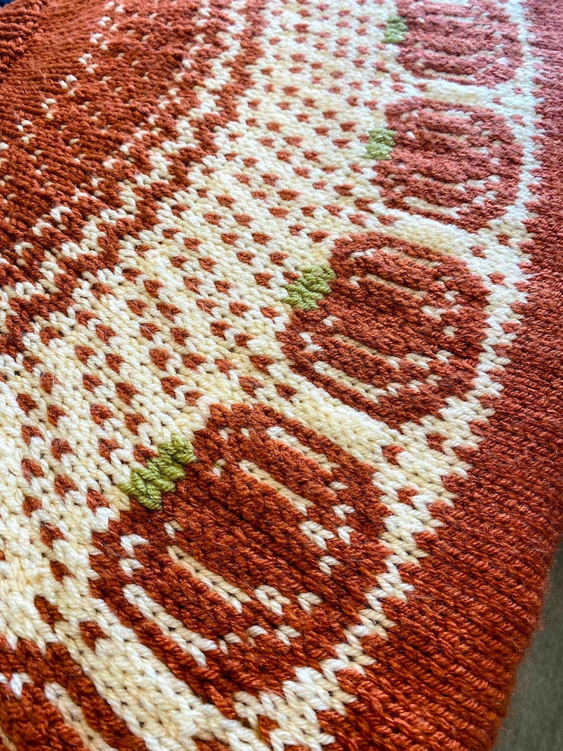 May include: Close-up of a knitted fabric with a brown, white, and green pattern. The fabric has a textured surface and a repeating design.