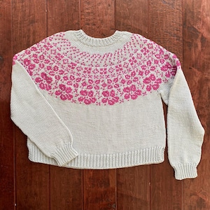 May include: A grey knitted jumper with a pink floral pattern around the neckline.