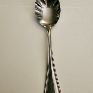 May include: A silver sugar spoon with a scalloped bowl and a simple, elegant handle.