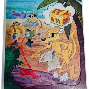 May include: A vintage Pitfall! frame-tray puzzle featuring a cartoon scene of adventurers on a beach with a treasure chest. The puzzle includes the text "FRAME-TRAY. Puzzle" and "Ages 3 to 7". The puzzle is made of cardboard.