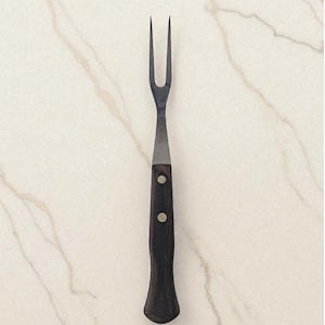 May include: A carving fork with a dark wooden handle and two tines. The handle is attached to a stainless steel blade with two rivets. The fork is designed for handling and serving roasted meats.