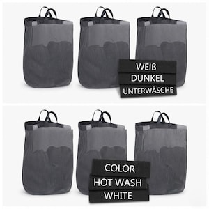 May include: Six dark gray mesh laundry bags with black handles. The bags are arranged in two rows of three. The image also includes black signs with white text that reads "WEIB, DUNKEL, UNTERWÄSCHE" and "COLOR, HOT WASH, WHITE."