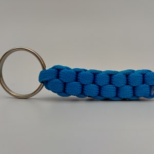 Puede incluir: Un llavero de paracord azul con un anillo de llave plateado.