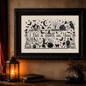 May include: A framed cross-stitch embroidery featuring black thread on a cream fabric background. The design includes the text "I Put a Spell on You" surrounded by Halloween motifs like a witch, cauldron, ghosts, bats, pumpkins, and an owl.