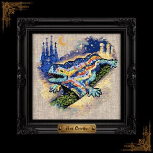 May include: A cross-stitch embroidery featuring a colorful, mosaic-patterned lizard positioned in front of a dark blue silhouette of a cathedral under a crescent moon and stars. The artwork is displayed in a black ornate frame with a gold plaque reading Ars Onirika.