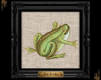 May include: A cross-stitch embroidery of a green frog with yellow eyes, positioned on a light beige linen fabric. The artwork is encased in a black ornate frame with a small gold-toned plaque at the bottom featuring the text Ars Onirika.