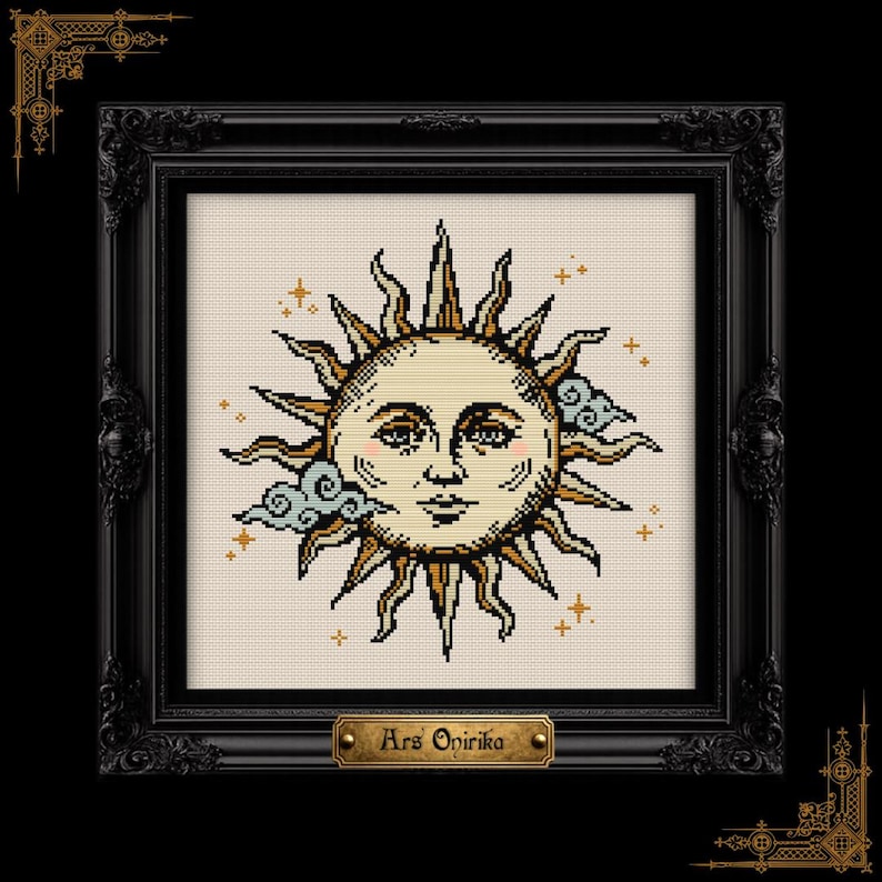 May include: A cross-stitch embroidery featuring a central sun face with golden rays, surrounded by small blue clouds and tiny star accents. The piece is enclosed in a black ornate frame with a gold-colored plaque at the bottom reading Ars Onirika.