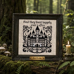 Può includere: Un ricamo a punto croce incorniciato su tessuto beige con la sagoma di un castello nero, volute ornamentali e il testo "And they lived happily ever after." Una piccola targhetta in ottone sulla cornice scura riporta "Ars Onirika."