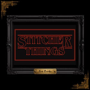 May include: A framed cross-stitch artwork featuring the text "STITCHER THINGS" in red, on a black backdrop. The black frame has decorative elements. A small brass plaque below reads "Ars Onirika".