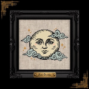 May include: A cross-stitch embroidery on light beige fabric featuring a central moon face with human features, surrounded by light blue stylized clouds and small orange stars. The piece is encased in a black ornate frame with a gold plaque reading Ars Onirika.