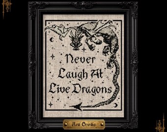 May include: A black and beige cross-stitch embroidery featuring a dragon illustration and the text "Never Laugh At Live Dragons" surrounded by small stars and crescent moons, encased in a black ornate frame with a gold plaque reading "Ars Onirika".