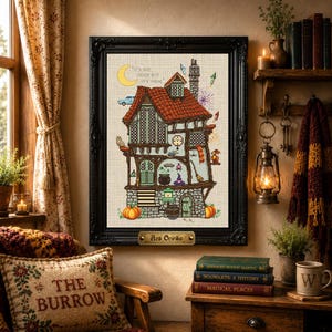 May include: A framed cross-stitch artwork depicting a multi-story house with a red roof, stone base, and various magical items including a cauldron, broom, and owl. The text "IT'S NOT MUCH BUT IT'S HOME" is stitched near a yellow crescent moon.