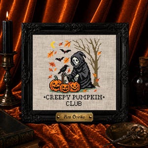 May include: A framed cross-stitch embroidery featuring a grim reaper figure, three orange jack-o'-lanterns, a black crow, bats, and falling autumn leaves. The text "CREEPY PUMPKIN CLUB" is stitched below the scene, with a brass plaque reading "Ars Onirika".