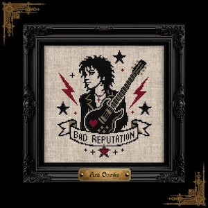 May include: A cross-stitch embroidery in a black ornate frame featuring a person with dark hair playing a black electric guitar. The design includes red lightning bolts, black stars, and a banner with the text BAD REPUTATION. A small gold plaque at the bottom reads Ars Onirika.