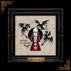 Puede incluir: Un bordado de punto de cruz en un marco negro que muestra a una persona con una larga trenza blanca y abrigo rojo, rodeada de tres dragones negros y verde azulado. El texto MOTHER OF DRAGONS está bordado, con una placa dorada Ars Onirika.
