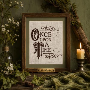 May include: A framed cross-stitch embroidery on light beige fabric featuring the dark brown text "Once Upon A Time" with decorative flourishes and small star accents. The wooden frame includes a small brass plaque labeled "Ars Onirika".