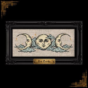 Puede incluir: Un bordado de punto de cruz con un motivo de triple luna, con una cara de luna llena central flanqueada por dos lunas crecientes, rodeadas de nubes azul claro y pequeñas estrellas doradas sobre tela beige, en un marco negro ornamentado con una placa que dice Ars Onirika.