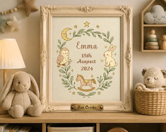 May include: A framed cross-stitch embroidery featuring a wreath of green leaves, a crescent moon, an owl, a rabbit, and a rocking horse. The centre text reads Emma, 13th August 2024. A small brass plaque at the bottom is engraved with Ars Onirika.