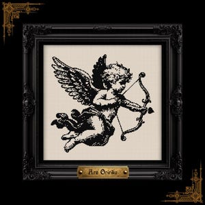 May include: A black and white cross-stitch pattern featuring a winged cherub holding a bow and arrow, set within an ornate black frame. A small gold-toned plaque at the bottom of the frame displays the text Ars Onirika in a dark serif font.
