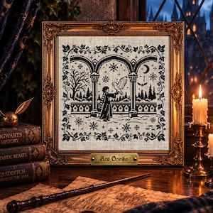 May include: A square cross-stitch embroidery in a gold ornate frame featuring a black silhouette design of a person holding an owl under stone arches, surrounded by winter trees, snowflakes, and a crescent moon, with the text Ars Onirika.