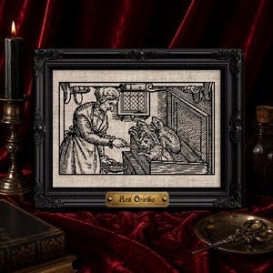 May include: A black framed embroidery piece featuring a black and white illustration of a person feeding creatures from a chest. The frame includes a small brass-colored plaque at the bottom with the text Ars Onirika engraved in black lettering.