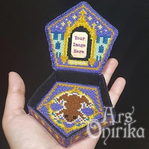 May include: A handcrafted, open box with a pentagonal lid and a square base. The box is made of cross-stitch fabric in shades of purple, gold, and blue. The lid features a rectangular frame with the text "Your Image Here". The base has a brown animal design.