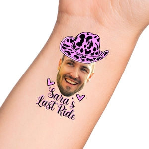 May include: A temporary tattoo with a pink and black cow print cowboy hat on a man's face. The text "Sara's Last Ride" is below the hat with two pink hearts.