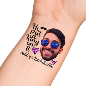 K&ouml;nnte beinhalten: Ein tempor&auml;res Tattoo mit dem Gesicht eines Mannes, der eine Sonnenbrille tr&auml;gt, und dem Text "He put a Ring on it Ashley's Bachelorette" mit einem rosa Diamanten und einem rosa Herzen.