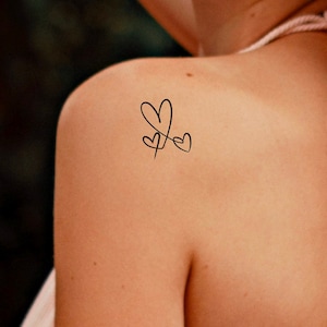 May include: A simple tattoo design of three intertwined hearts on a person's shoulder.