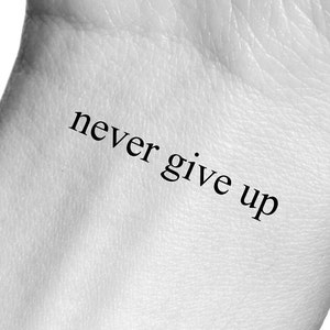 Może przedstawiać: Zbliżenie na nadgarstek osoby z tymczasowym tatuażem z napisem "never give up".