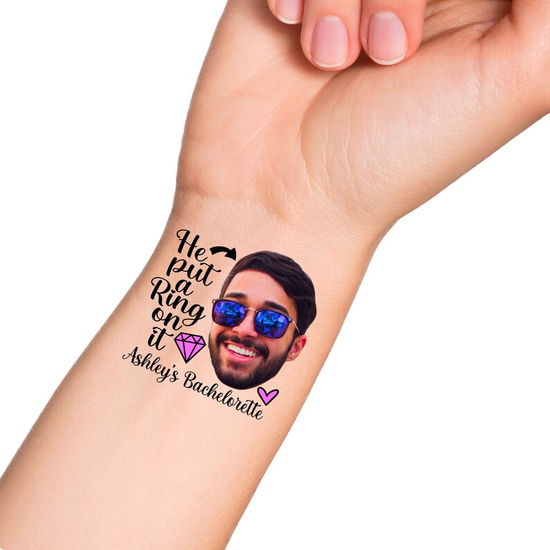 K&ouml;nnte beinhalten: Ein tempor&auml;res Tattoo mit dem Gesicht eines Mannes, der eine Sonnenbrille tr&auml;gt, und dem Text "He put a Ring on it Ashley's Bachelorette" mit einem rosa Diamanten und einem rosa Herzen.
