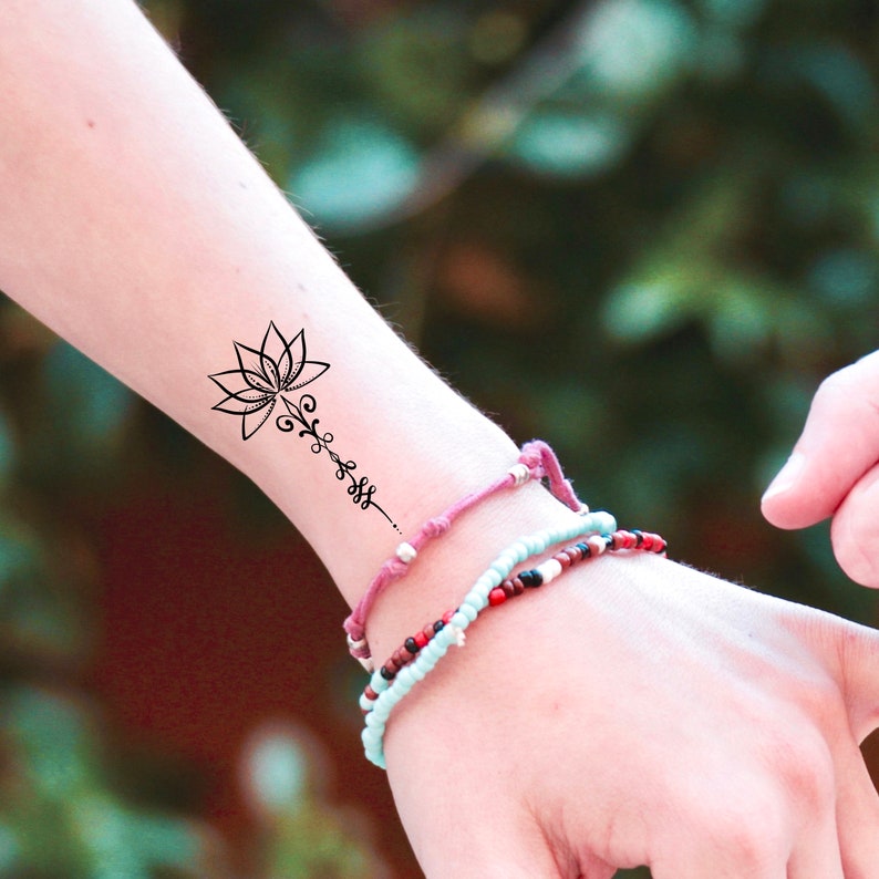 K&ouml;nnte beinhalten: Ein schwarzes und wei&szlig;es tempor&auml;res Tattoo einer Lotusblume mit einem Rankendesign auf dem Handgelenk einer Person.