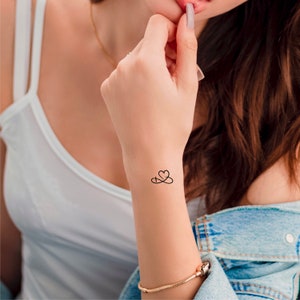 Pu&ograve; includere: Un tatuaggio temporaneo di un simbolo di infinito con un cuore al centro, applicato sul polso di una persona.