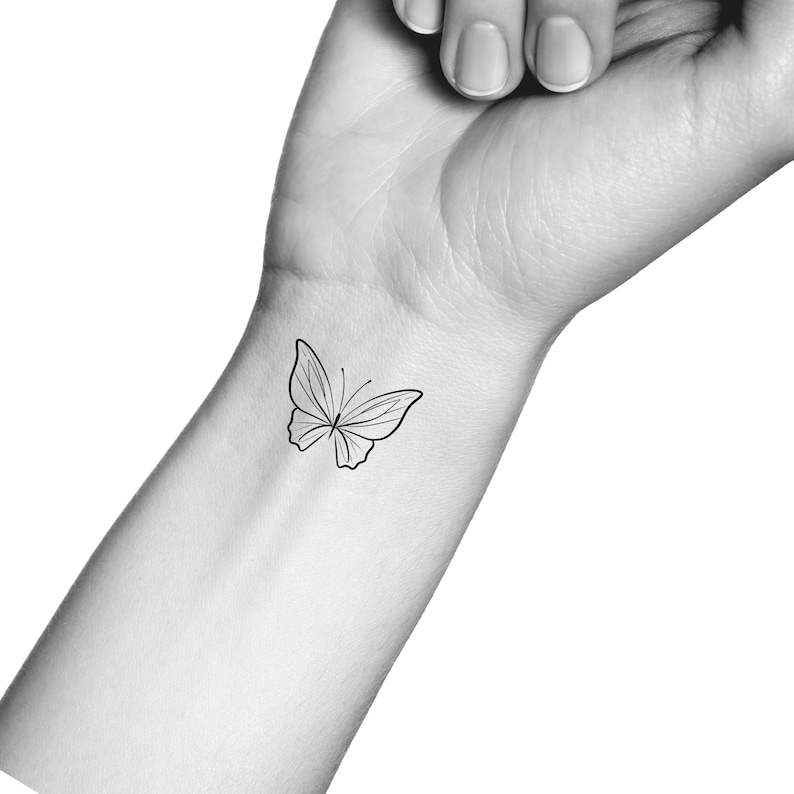 Op de afbeelding: Een eenvoudige lijntekening van een vlinder-tattoo op de pols van een persoon.