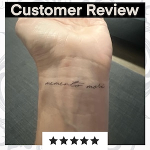 May include: A customer review of a temporary tattoo with the text "memento mori" in cursive script. The tattoo is applied to the wrist of a person. The review is 5 stars.