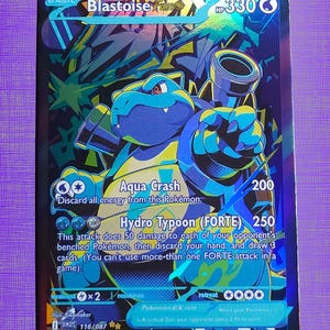 May include: A holographic Blastoise FORTE trading card with 330 HP. The card features a blue Blastoise character with cannons, displaying the attacks Aqua Crash and Hydro Typoon (FORTE). The background has a vibrant, multi-colored graffiti-style design.