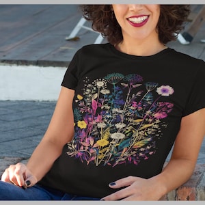 Peut inclure: Un t-shirt noir avec un imprim&eacute; floral color&eacute;. Les fleurs sont dans des tons de rose, violet, jaune et bleu. L'impression est un motif stylis&eacute; d'un bouquet de fleurs sauvages.