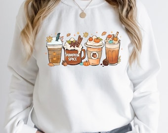 May include: White sweatshirt featuring a colorful graphic of four different fall-themed coffee drinks. The design includes pumpkins, leaves, and the words "Pumpkin Spice" on a mug. The sweatshirt is a cozy, casual style.