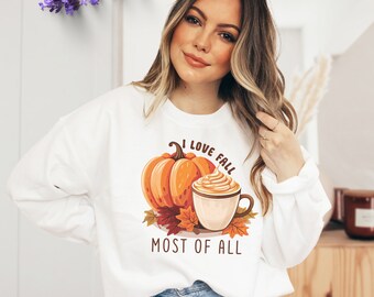 May include: White sweatshirt with a fall-themed graphic. The design features an orange pumpkin, a cup of coffee with whipped cream, and the text "I LOVE FALL MOST OF ALL".