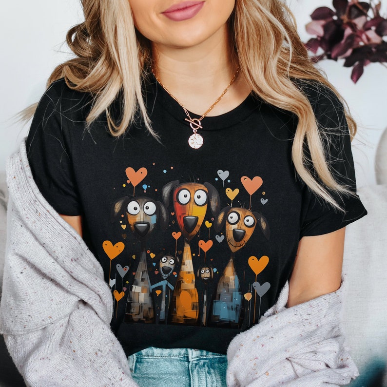 May include: A black t-shirt with a graphic print of four cartoon dogs with hearts and colorful paint splatter details. The dogs are standing in a row and have different colored fur and eyes. The background is black.