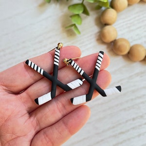 K&ouml;nnte beinhalten: Ein Paar schwarze und wei&szlig;e Hockey-Schl&auml;ger-Ohrringe mit goldenen Akzenten. Die Ohrringe sind aus Polymer Clay gefertigt und sollen wie Hockeyschl&auml;ger aussehen.