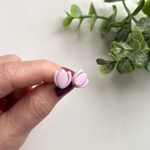 Puede incluir: Un par de pendientes de bot&oacute;n de color rosa en forma de flor. Los pendientes est&aacute;n hechos de arcilla polim&eacute;rica y tienen un acabado mate.