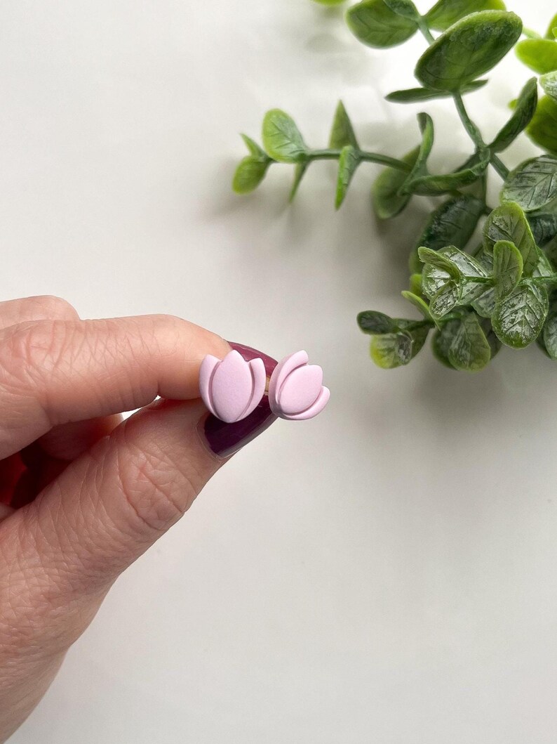 Puede incluir: Un par de pendientes de bot&oacute;n de color rosa en forma de flor. Los pendientes est&aacute;n hechos de arcilla polim&eacute;rica y tienen un acabado mate.